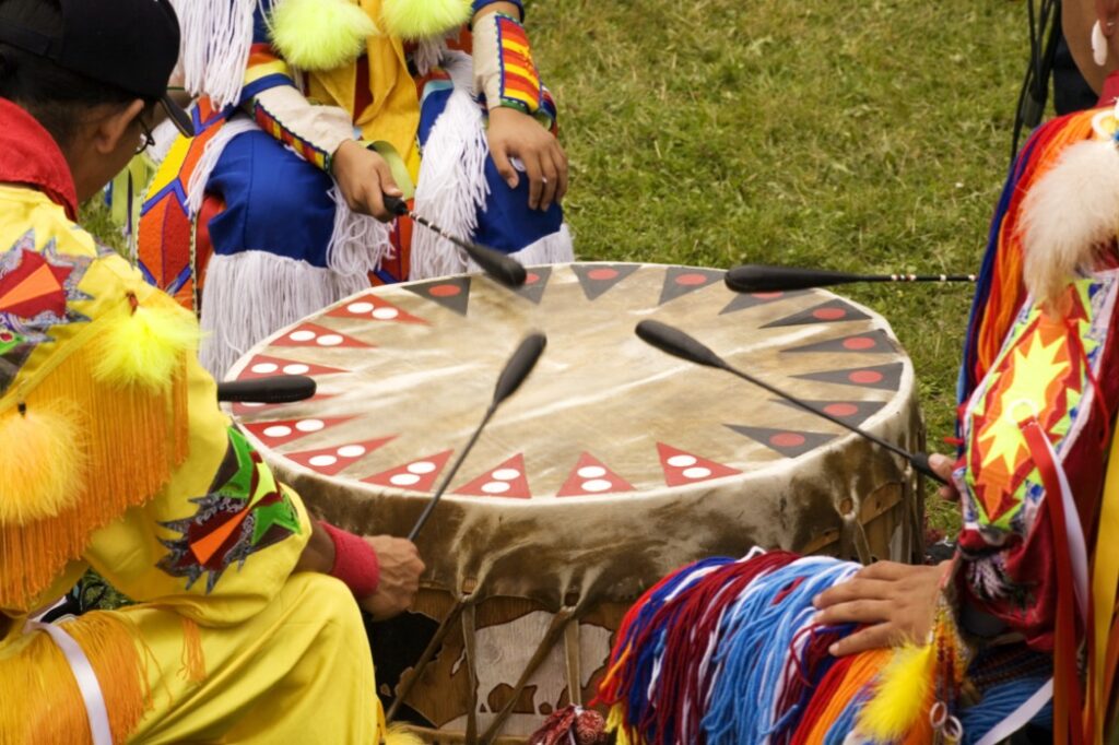 First nations in traditional dress playing drum